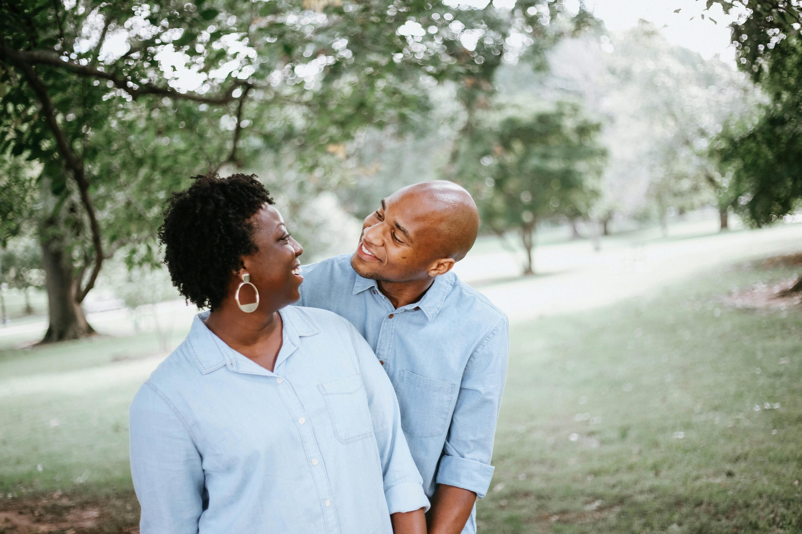 Happy couple enjoying a playful moment together in a sunny park setting.
