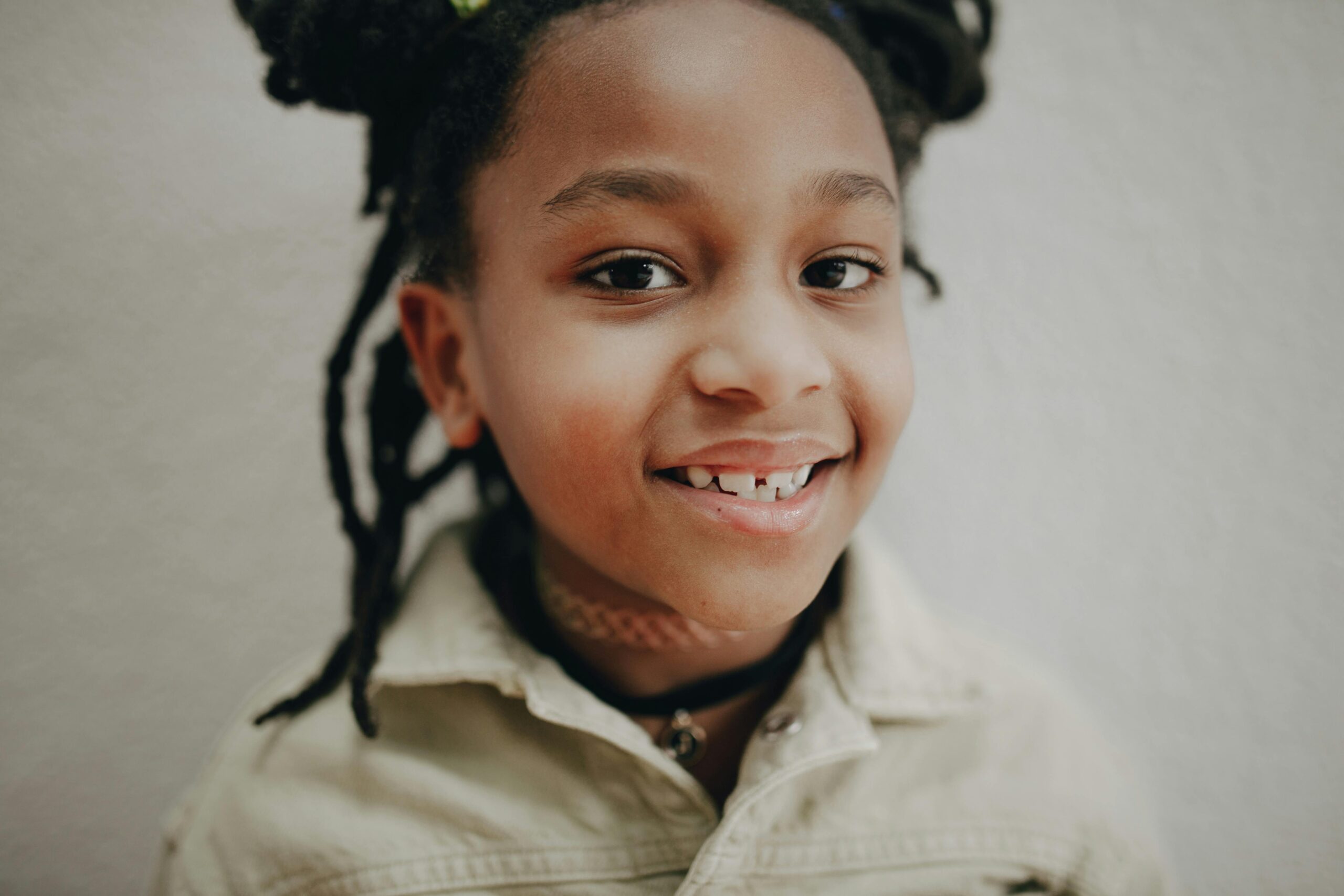 Close-up headshot of a smiling child with afro pigtails and a playful expression.