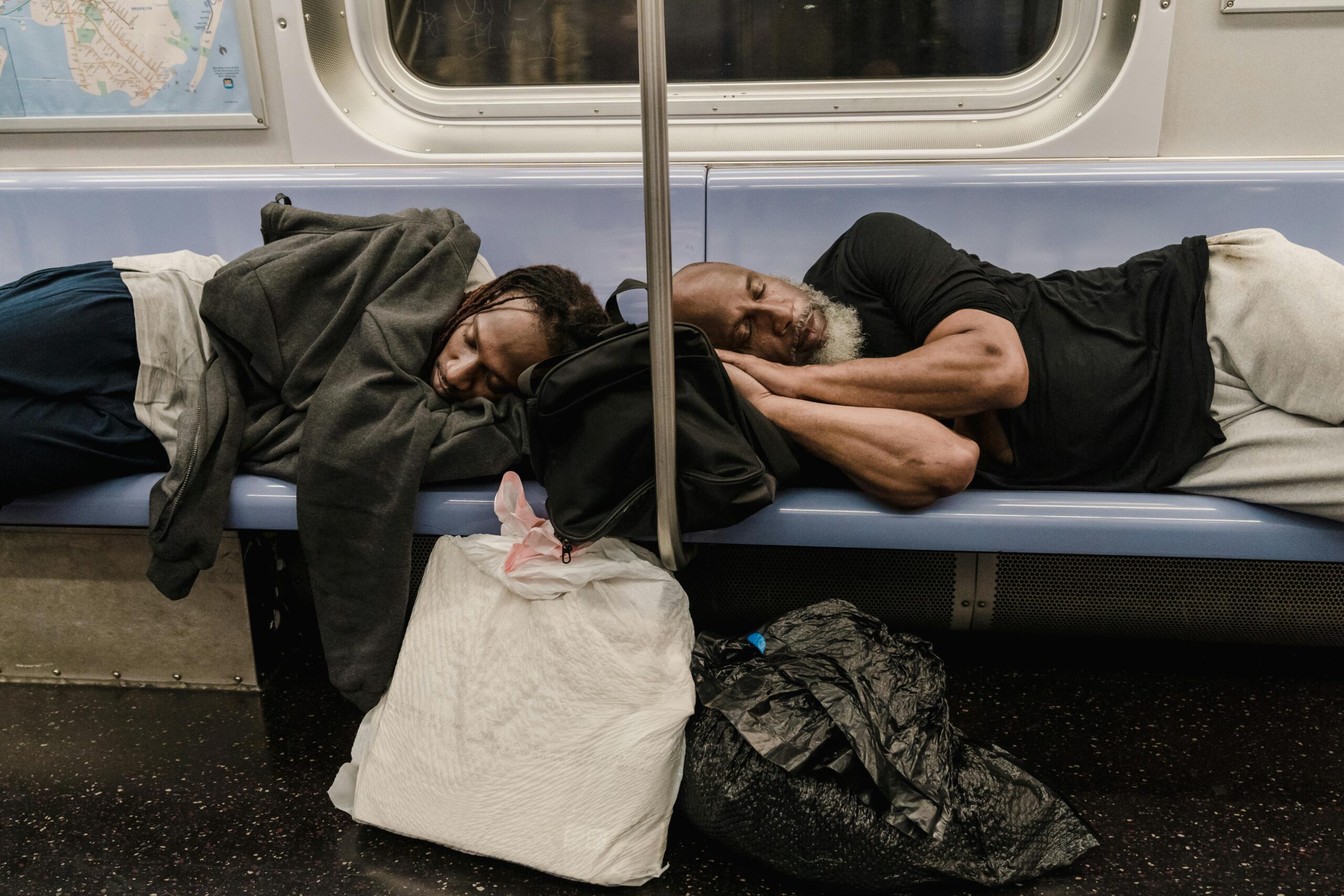 Two adults rest on a subway bench surrounded by bags, illustrating urban life.